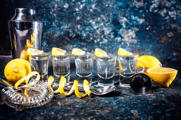 Tiros de tequila de plata con rodajas de limón y elementos de cóctel. Bebidas alcohólicas en vasos de chupito servidos en pub o bar —  Fotos de Stock