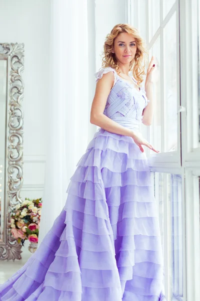 curly blonde in an elegant luxury purple dress in a light clean empty room
