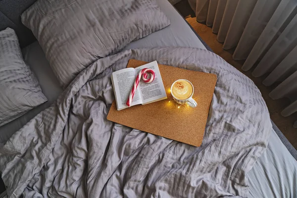Dormitorio con cama grande en colores beige, taza de café, caña de caramelo de menta y libro —  Fotos de Stock
