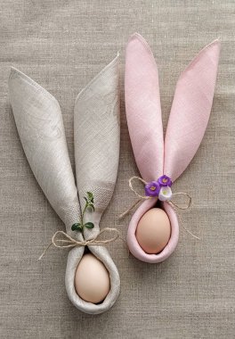 İki dekoratif tavşan kulağı peçeteden, doğal pamuk masa örtüsü üzerine yumurtayla Paskalyayı kutlamak için.