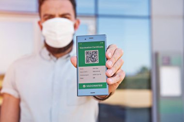 Covid-19 için mobil uygulamalı dijital yeşil aşı sertifikası sunan akıllı telefonu tutan bir adam. Dokunulmazlık aşısı pasaportu, aşı sertifikası, yeni normal seyahat için sağlık pasaportu