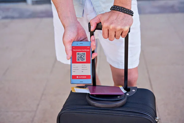 Suitcase and smartphone in hand displaying on app mobile expired digital vaccination certificate for Covid-19. Immunity vaccine passport, vaccination certificate, health passport for travel