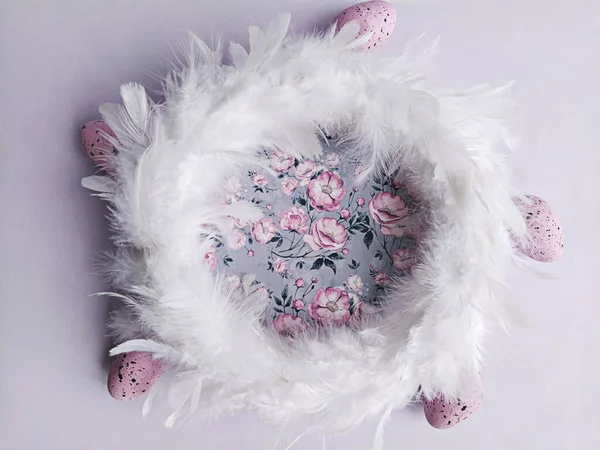 Witte veren krans op lila bloemige achtergrond met decoratieve paaseieren, bovenaanzicht — Stockfoto