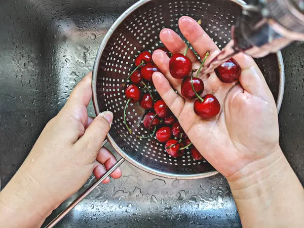 La baya madura de las cerezas frescas en el tamiz de acero se lava a mano bajo el agua del grifo en el fregadero — Foto de Stock