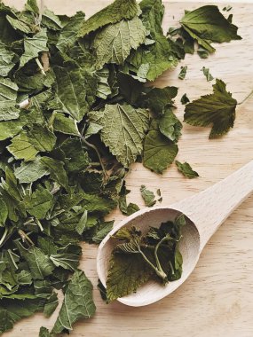 Tahta kaşık ve yiyeceğin üzerinde kurumuş kuşüzümü yaprakları, kırsal mutfak dokusu ve güzel kokulu bitki çayı havası.