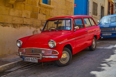 Taştan binalar ve mavi kapının yanında kırmızı Ford steyşın vagonun ön üç çeyrek manzarası: Xghajra, Malta - 7 Haziran 2021