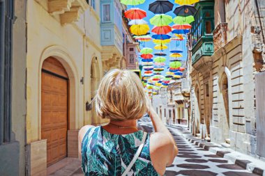Güneşli, mavi gökyüzü olan eski kasaba caddesinde asılı şemsiye altında fotoğraf çeken kadının arka görüntüsü