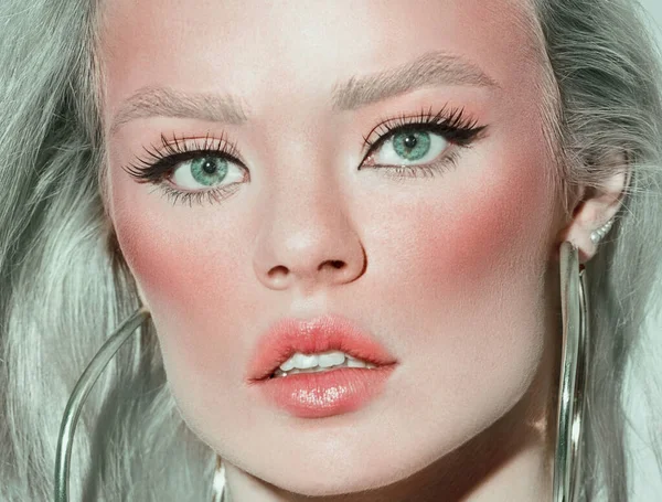 Close-up of a woman's face. Long eyelashes and eyelashes. Blond hair with a green tint. Beautiful natural makeup.