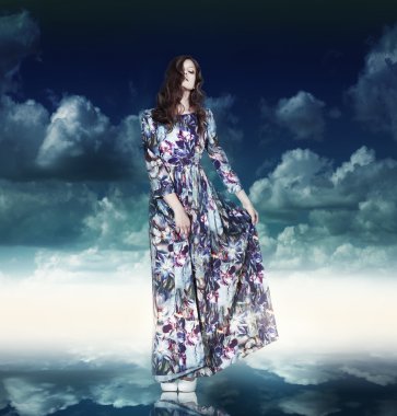Fantasy. Luxurious Woman in Variegated Dress over Blue Sky clipart