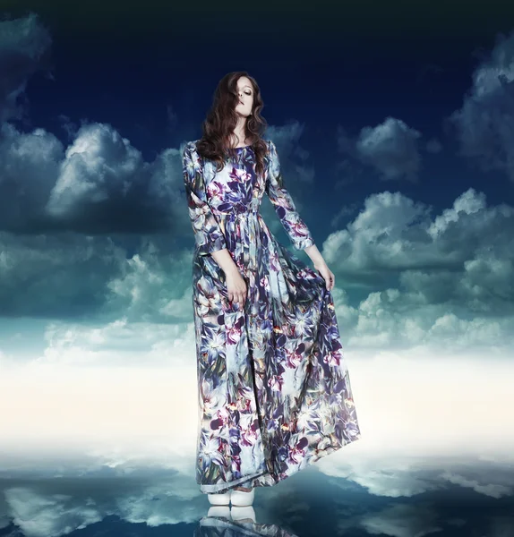 Fantasie. Luxe vrouw in bonte jurk over blauwe hemel — Stockfoto