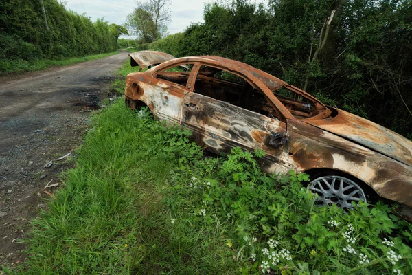 Quemado coche viejo oxidado empujado fuera de la carretera en el borde de la hierba — Foto de Stock