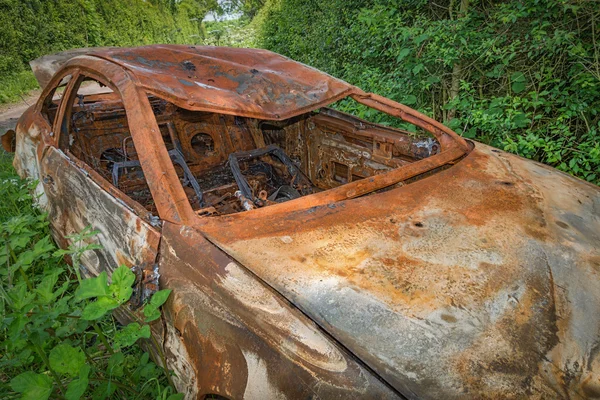 Сгоревшая ржавая машина, оставленная в листве на обочине дороги — стоковое фото