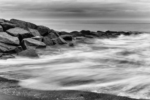 Vagues laiteuses éclaboussant les rochers en noir et blanc — Photo