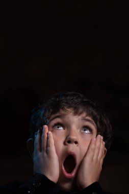 Karanlıkta çığlık atan korkmuş küçük bir çocuk. Çığlık atan surat. Yukarı bakıyor..