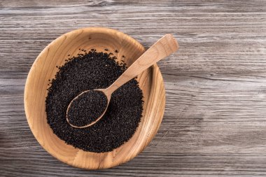 Kurumuş kimyon tohumlarının düz yatağı. Ahşap tabakta kalinji. Kırsal gri arka planda tahta kaşık..