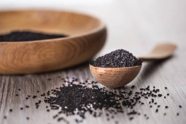 Kurumuş kimyon tohumlarını yakın plan çekimde ahşap kaşık üzerinde kalinji ve arka planda ahşap plaka. Yumuşak odak.