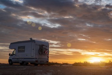 Gün batımı / gün doğumu Rocky Sahil 'de seyahat karavanıyla. Güneş ışınlarıyla dramatik ve sakin bulutlu gökyüzü.