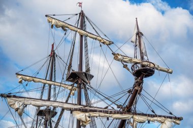 Bulutlu mavi gökyüzünün arka planında eski bir korsan gemisinin direkleri ve donanımı.