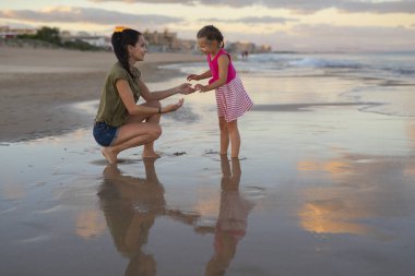 Mutlu bir aile. Genç mutlu anne ve kızı gün batımında sahilde eğleniyorlar. Olumlu insani duygular, duygular.