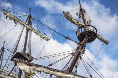 Bulutlu mavi gökyüzünün arka planında eski bir korsan gemisinin direkleri ve donanımı.