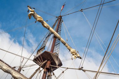 Bulutlu mavi gökyüzünün arka planında eski bir korsan gemisinin direkleri ve donanımı.