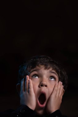 Karanlıkta çığlık atan korkmuş küçük bir çocuk. Çığlık atan surat. Yukarı bakıyor..