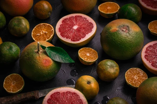 Low key side view of citrus fruits background. Mix of cutted grapefruits and mandarins. Composition with selective focus.