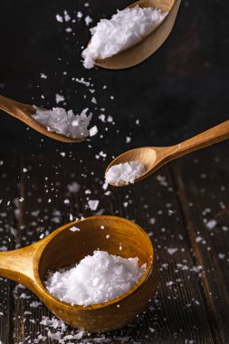 Spilled sea salt in crystals on wooden spoons closeup. Close up Low key composition on dark rustic wooden background. Selective focus