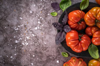 Whole and sliced organic tomatoes Raf Coeur De Boeuf. Raw fresh tomatos with sea salt and basil on rustic dark metal texture background. Top view with copy space