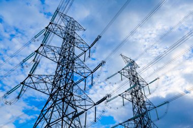 Mavi gökyüzü bulutlarına karşı elektrik direği, kırsal alana elektrik aktarım hattı.