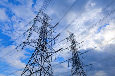 Mavi gökyüzü bulutlarına karşı elektrik direği, kırsal alana elektrik aktarım hattı.