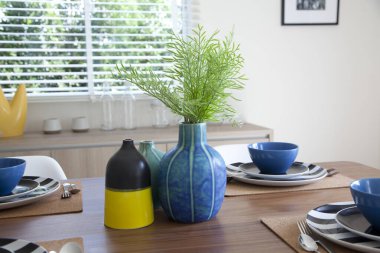 Modern evdeki dekoratif vazo ile yemek masasında modern tabak seti..