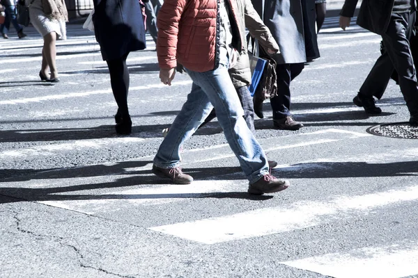 Unrecognizable and blurry people crossing the road at a pedestrian crossing. Close-up at legs.