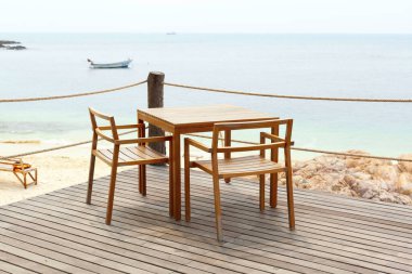 Ahşap masalar ve bir bar veya restoran terasında denize bakan sandalyeler.