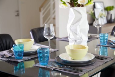 Modern evin siyah yemek masasında mavi ve yeşil tabak seti ve bir buket çiçek..