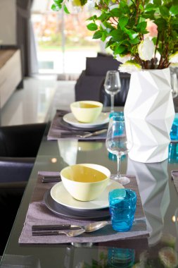 Modern evin siyah yemek masasında mavi ve yeşil tabak seti ve bir buket çiçek..