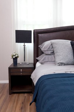 Mavi ve siyah yastıklı, komodinin üzerinde siyah okuma lambası olan modern tarz iç yatak odası..