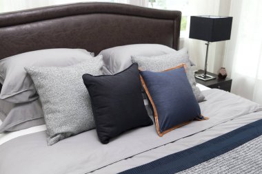 Mavi ve siyah yastıklı, komodinin üzerinde siyah okuma lambası olan modern tarz iç yatak odası..