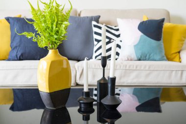 İskandinav oturma odasının iç kısmında kahve masası olan beyaz bir koltukta mavi ve sarı yastıklar..