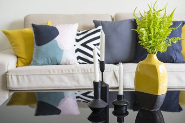 İskandinav oturma odasının iç kısmında kahve masası olan beyaz bir koltukta mavi ve sarı yastıklar..