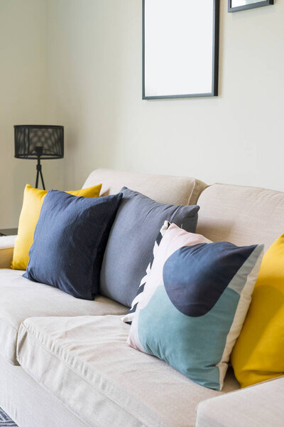 Blue and yellow pillows on a white sofa with coffee table in Scandinavian living room interior.