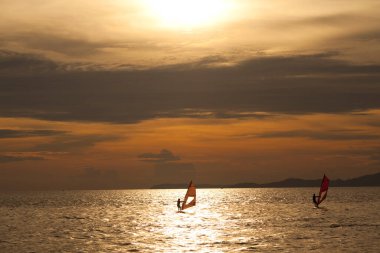 Güzel gün batımında körfezin dalgalarında sörf yapan bir adamın silueti..
