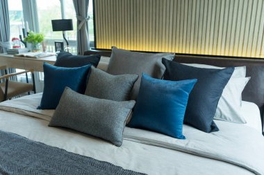 Yatağında gri ve mavi yastıklar olan şık bir yatak odası, rahat iç tasarım, modern iç mimari.