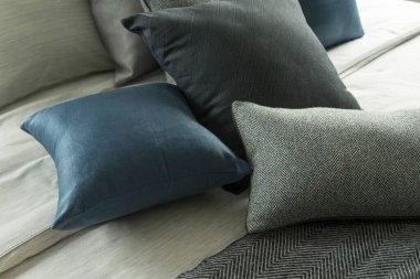 Yatağında gri ve mavi yastıklar olan şık bir yatak odası, rahat iç tasarım, modern iç mimari.