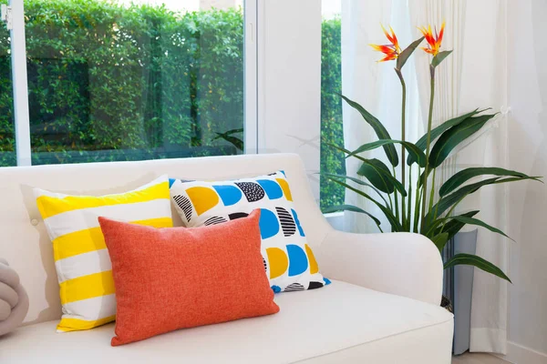 Oturma odasının içi yeşil bitkilerle süslenmiş. Kırmızı ve sarı yastıklı, rahat bir kanepe..