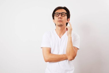 Beyaz tişörtlü ve gözlüklü yakışıklı, orta yaşlı Asyalı adam beyaz arka planda izole edilmiş bir şekilde düşünüyor ve bakıyor.