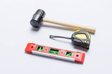 Beyaz arkaplanda inşa araçları, lastik çekiç, metre ve balon seviyesi.