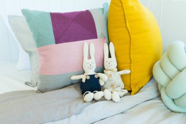 Yatağın üzerinde renkli yastıklarla duran tavşan bebekleri.