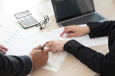 Kadın ve erkeğin ofis masasında oturup iş planlarını tartışırken bir belge imzalaması..