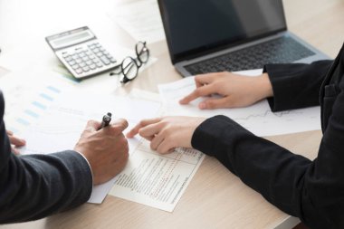 Kadın ve erkeğin ofis masasında oturup iş planlarını tartışırken bir belge imzalaması..